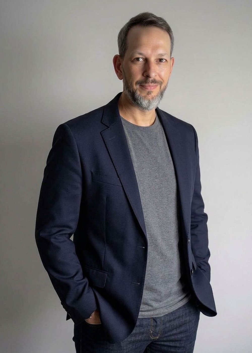 Alan Prachar wearing a navy blazer and gray T-shirt against a neutral background.